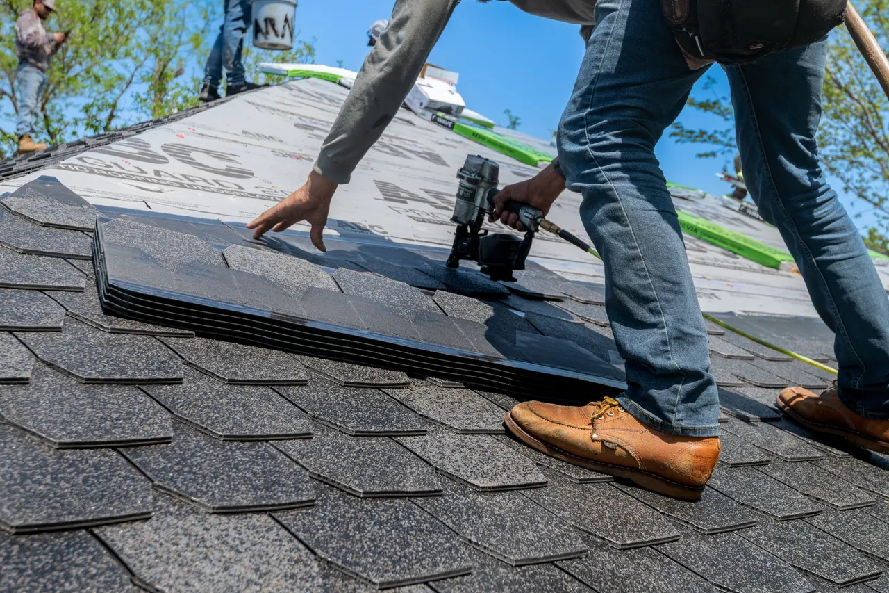 A roofer laying asphalt shingles on a new roof